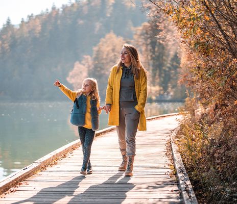 Mutter und Kind gehen Hand in Hand über einen Holzsteg am See im Herbstlicht