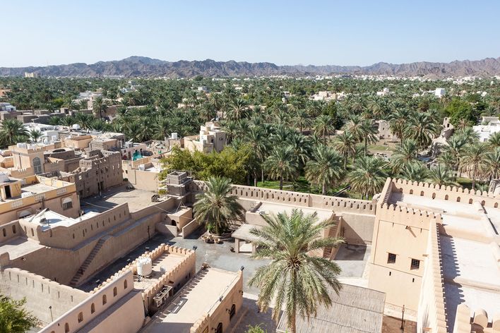 Blick auf die Stadt Nizwa mi Oman mit Lehmhäusern, Palmen und Oasenlandschaft