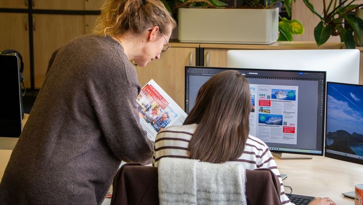 Ausbilderin Manuela erklärt der Auszubildenden Charlotte etwas in einem Katalog