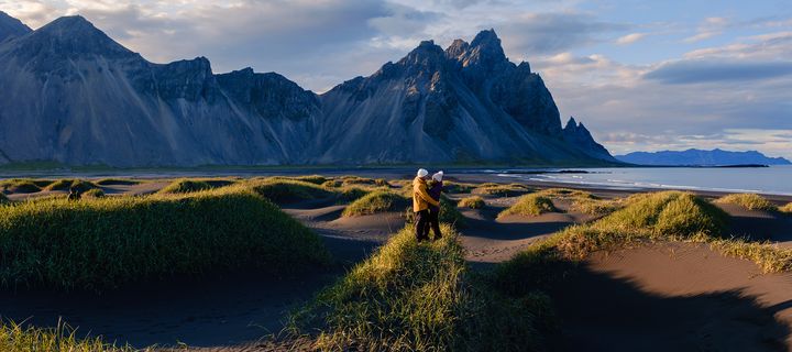 Paar in der Landschaft von Stokksnes auf Island bei Sonnenschein mit Dünen, Strand und Bergkulisse