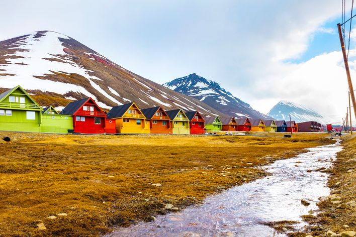 Blick auf mehrere Holzhütten in den Spitzbergen mit Bergen im Hintergrund
