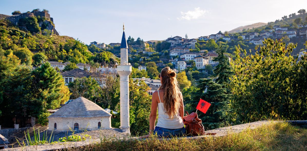 Frau sitzt vor den Toren der historischen Altstadt von Gjirokastra, eine weitere UNESCO-Weltkulturerbestätte mit charakteristischen Häusern und Festung