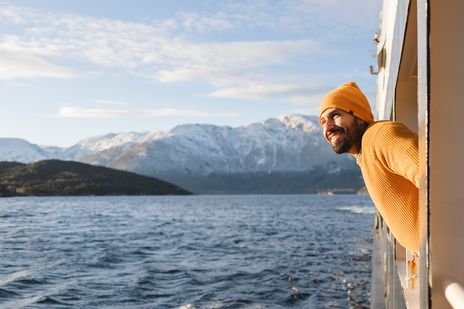 Ein lächelnder Mann lehnt sich aus einem Schiff und bewundert die wunderschöne verschneite Berglandschaft