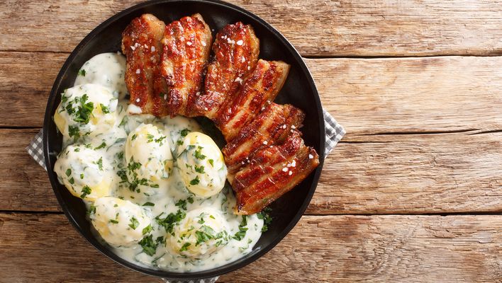 Dänisches Stegt Flæsk mit Kartoffeln, Petersiliensoße und knusprigem Schweinefleisch wird in einer Pfanne serviert