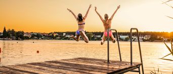 Zwei Frauen  die bei Sonnenuntergang in einen Badesee springen