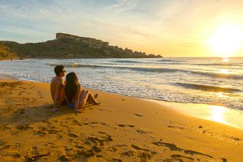 Ein Paar beobachtet den Sonnenuntergang am Strand von Ghajn Tuffieha Bay, Malta