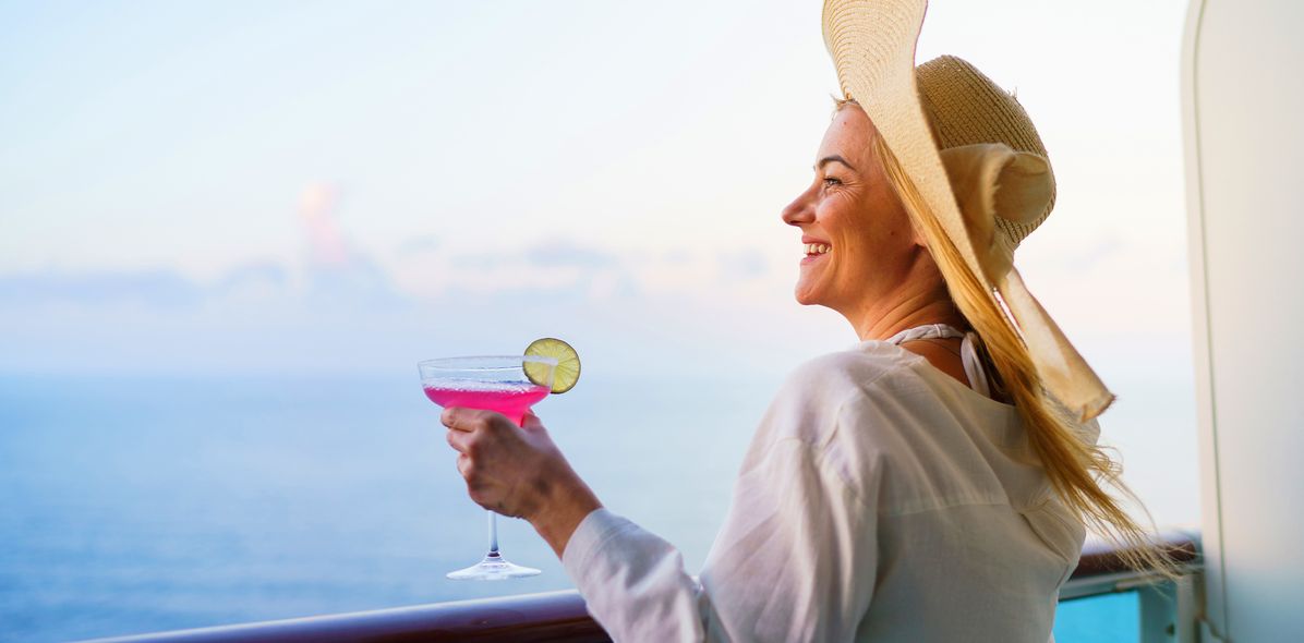 Eine Frau auf dem Balkon eines Kreuzfahrtschiffes genießt ihren Cocktail