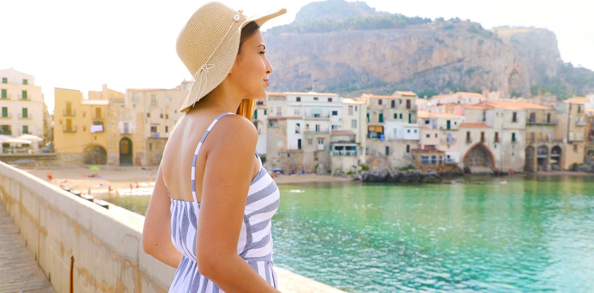 Frau mit Hut am Hafen von Cefalù mit Blick auf das Meer
