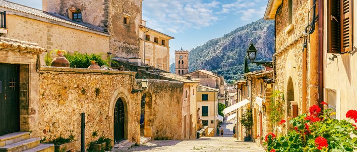 Steingasse in Pollença auf Mallorca mit alten Häusern und roten Blumen