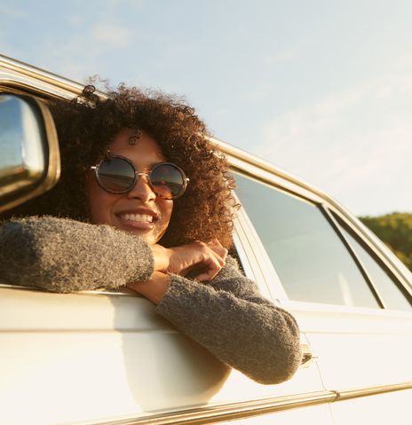 Frau mit Sonnenbrille lehnt sich aus ihrem Autofenster