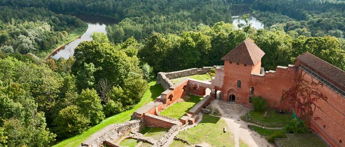 Burg Sigulda in Lettland umgeben von grünen Wäldern und hügeliger Landschaft