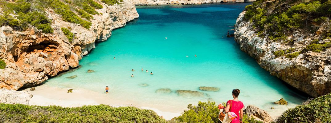 Frau blickt auf die Badebucht Calo des Moro mit türkisfarbenem Wasser und Felsen