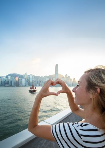Frau formt Herz mit den Händen vor der Skyline von Hongkong