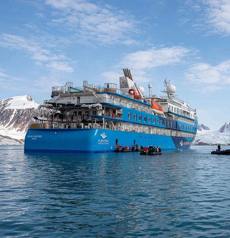 Blick von seitlich hinten auf das Expeditionsschiff Ocean Albatros auf dem Meer vor Grönlands Eisbergen