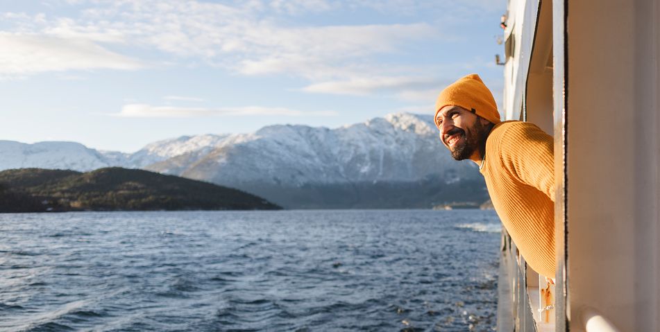 Ein lächelnder Mann lehnt sich aus einem Schiff und bewundert die wunderschöne verschneite Berglandschaft
