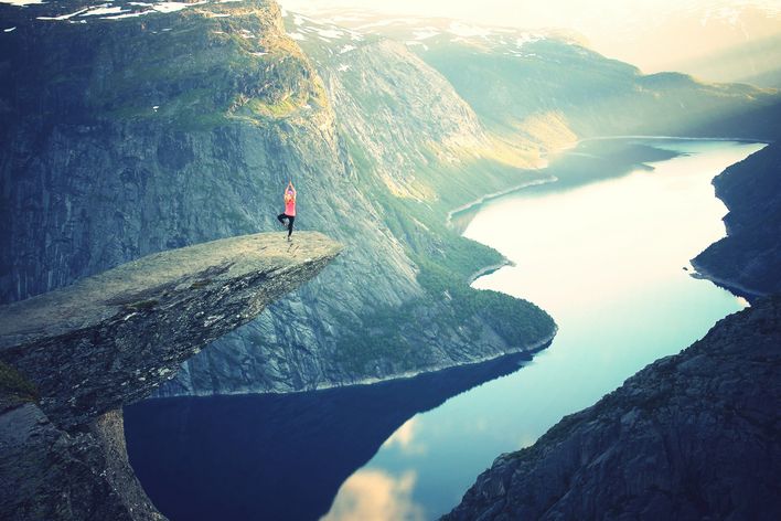 Eine Person steht auf der Trolltunga und im Hintergrund sind Berge, Fjorde und Gletscher zu sehen