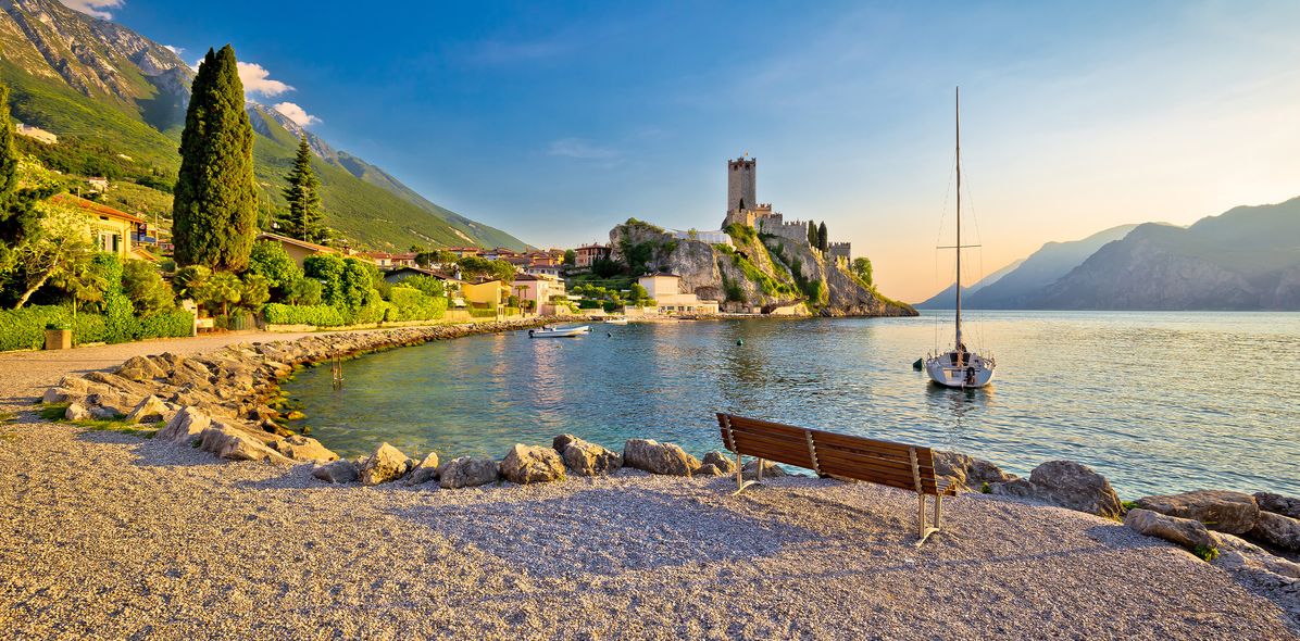 Strand in Malcesine am Gardasee mit Blick auf die Scaligerburg und Segelboot bei Sonnenuntergang