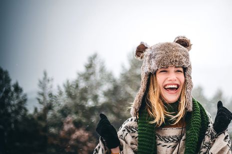 Frau mit Wintermütze steht fröhlich in winterlicher Landschaft