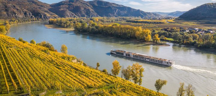 Flusskreuzfahrtschiff fährt entlang der Donau in Österreich mit Weinbergen am Ufer