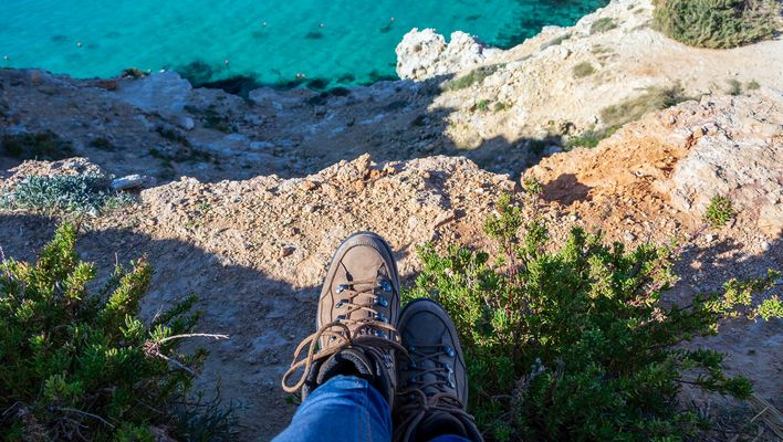 Wanderer sitzt mit Blick auf die Klippen und das Meer unter den Füßen