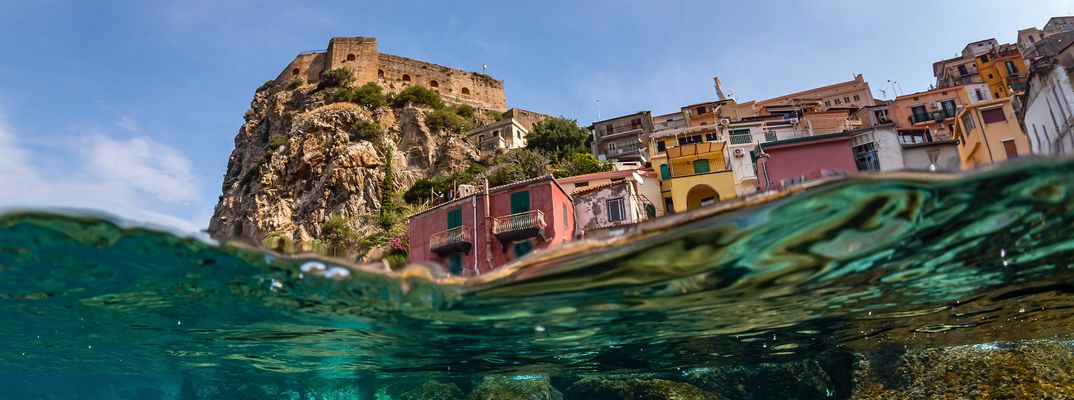 Geteilte Unterwasseraufnahme von Scillas Küste mit Felsen und bunten Häusern
