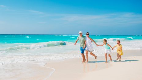 Eine Familie mit zwei Kindern läuft fröhlich durch die Wellen am Strand