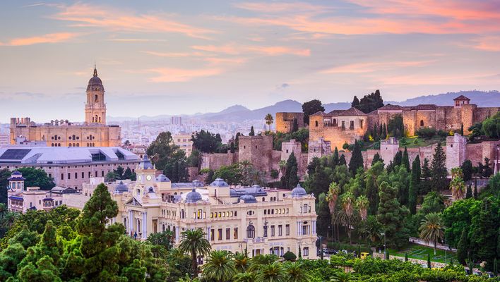 Panoramablick auf Málaga mit der Kathedrale, historischen Gebäuden und umliegenden Hügeln im warmen Licht des Sonnenuntergangs