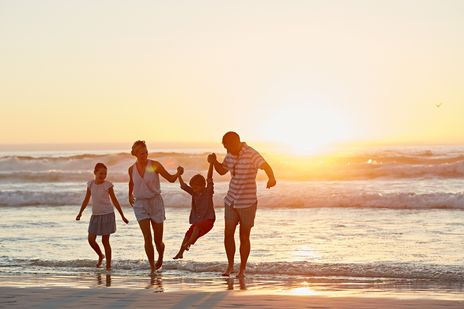 Familie läuft Hand in Hand am Strand entlang bei Sonnenuntergang