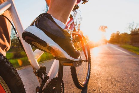 Ausschnitt von Fahrradpedalen mit Schuh mit Blick in Fahrtrichtung dem Sonnenaufgang entgegen
