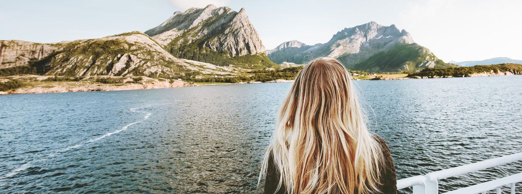 Eine Frau die an Bord eines Schiffes ist und auf Berge in Norwegen schaut