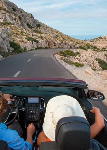 Personen fahren im Cabrio am Cap de Formentor eine Küstenstraße entlang, Blick aufs Meer