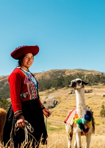 Frau in traditioneller Kleidung steht mit Alpakas auf einer Wiese in Peru