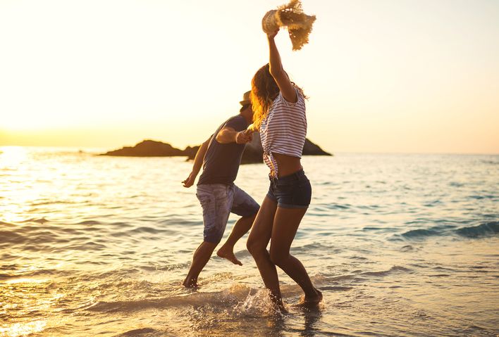 Fröhlich tanzendes Paar am Meer bei Sonnenuntergang