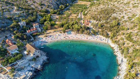 Luftaufnahme der Bucht Dubovica auf der Insel Hvar in Kroatien mit Kiesstrand, Steinhäusern und klarem Wasser