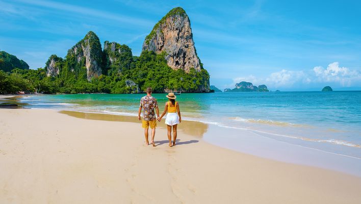Paar händchenhaltend von hinten am Strand von Krabi in Thailand mit Blick auf das Meer und Felsen im Hintergrund 