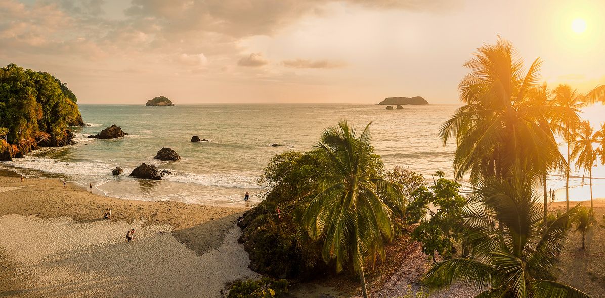 Tropischer Strand in Costa Rica bei Sonnenuntergang mit Palmen und Felsen am Wasser
