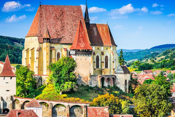 Die Kirchenburg von Biertan steht mit roten Dächern auf einem Hügel zwischen grünen Bäumen.