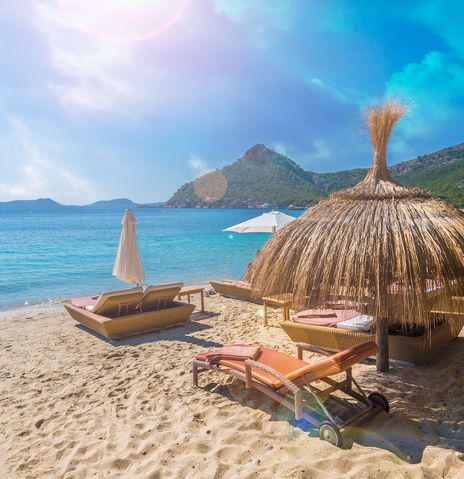 Strand bei Can Picafort auf Mallorca mit Sonnenschirmen aus Stroh, Liegen und Blick aufs Meer