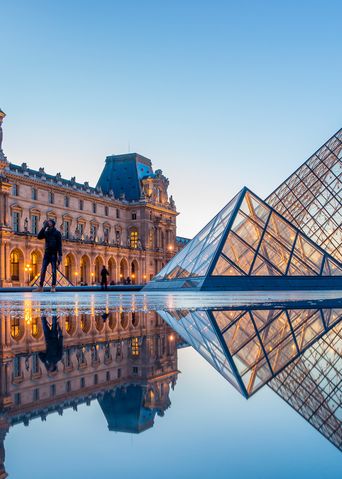 Louvre in Paris mit Glaspyramide und historischer Museumsfassade bei Sonnenuntergang