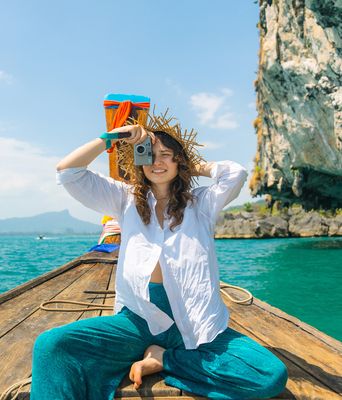 Eine Frau sitzt in einem typischen thailändischen Boot in einer Bucht und fotografiert in die Kamera