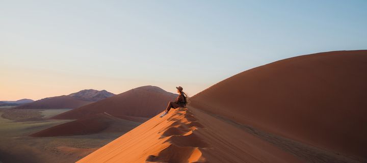 Frau sitzt in der Wüste im Namib Naukluft Nationalpark in Namibia und genießt den Ausblick