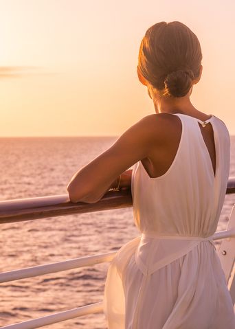 Frau an einer Schiffsreling und blickt in den Sonnenuntergang