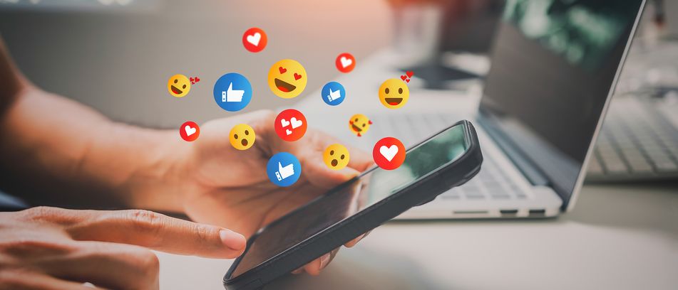 Mann hält Smartphone in der Hand mit Emojis über dem Display 