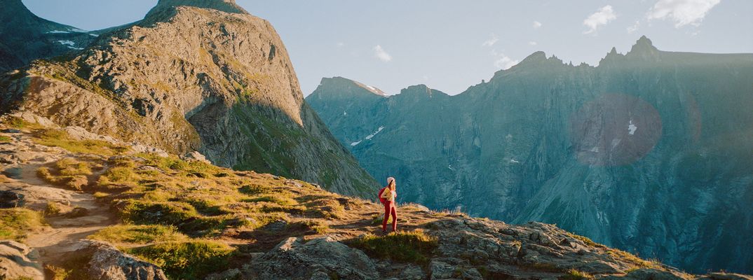 Wanderer marschiert über Felsen mit Blick auf Bergspitzen in den Alpen bei Sonnenlicht