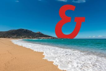 Ein Strand an der Küste von Korsika mit einem Dorf im Hintergrund und dem Berge & Meer Superzeichen