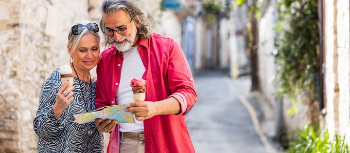 Älteres Paar betrachtet eine Landkarte in enger Altstadtgasse, beide halten ein Eis in der Hand