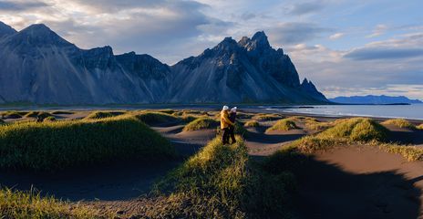 Paar in der Landschaft von Stokksnes auf Island bei Sonnenschein mit Dünen, Strand und Bergkulisse