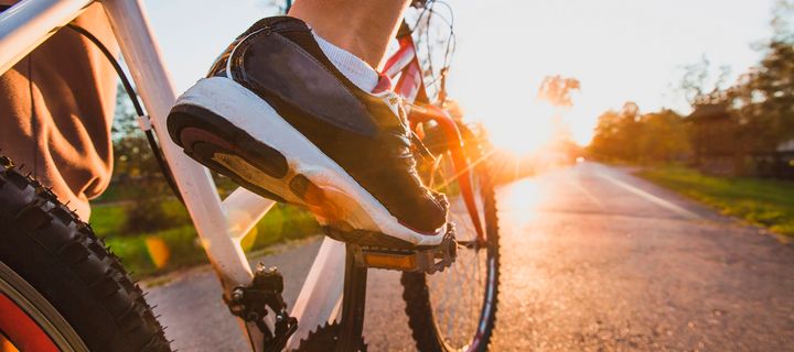 Ausschnitt von Fahrradpedalen mit Schuh mit Blick in Fahrtrichtung dem Sonnenaufgang entgegen