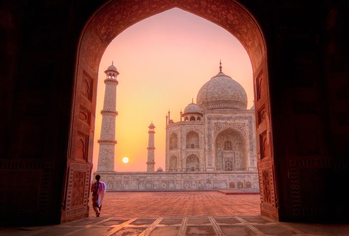 Frau steht beim Sonnenuntergang in einem Torbogen mit Blick auf den Taj Mahal, Indien