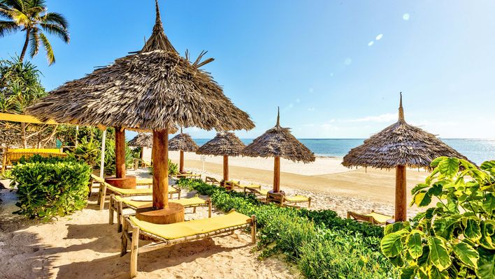 Blick aufs Meer von Sansibar über einen typischen Strand mit Sonnenschirmen und -liegen aus Palmen und Bäumen